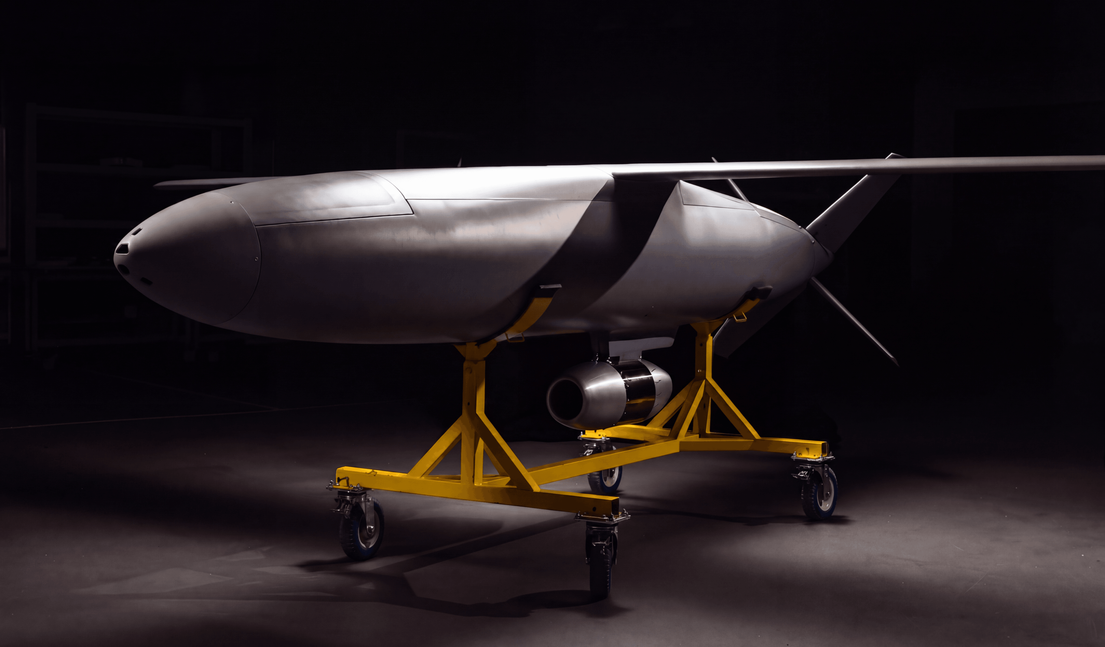 The full Covenant airframe on a yellow wheeled cradle in a darkened hangar, wings and tail extended, engine mounted beneath the fuselage.